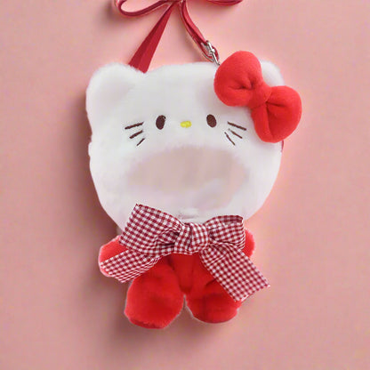 A plush doll wearing a white outfit with red accents, including a bow and a hat resembling a cat, hanging from a red ribbon.