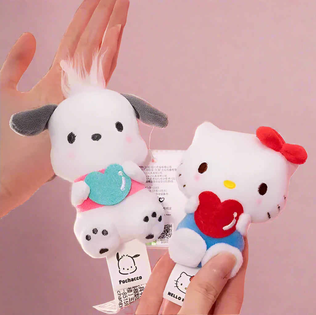 Two plush keychains featuring characters from Sanrio, one designed like a white cat with a blue heart and the other like a white bear with a red heart.