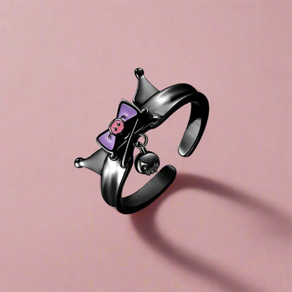 Black open ring with purple bow, pink heart, and skull charm on a white background