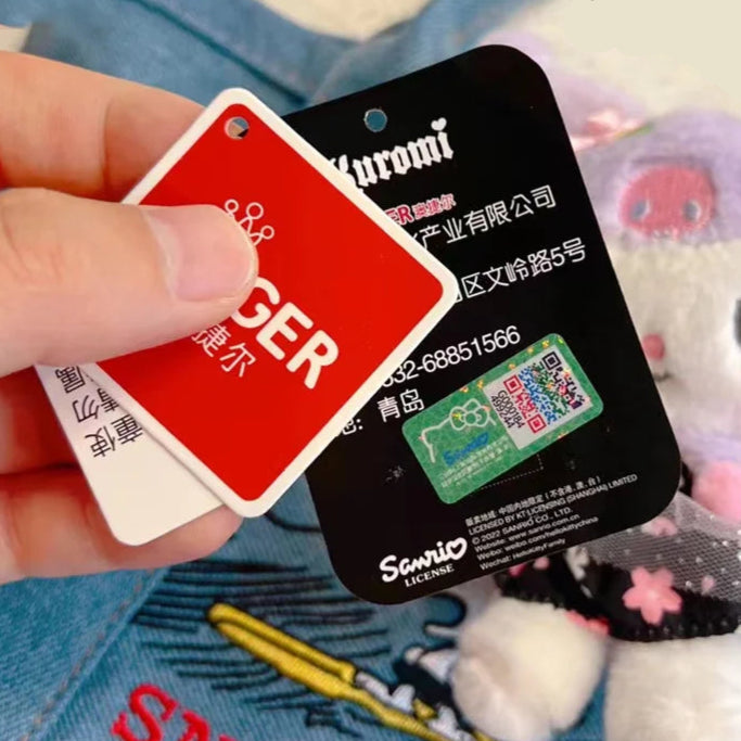 Hand holding a red and black card with branding, plush toy in the background