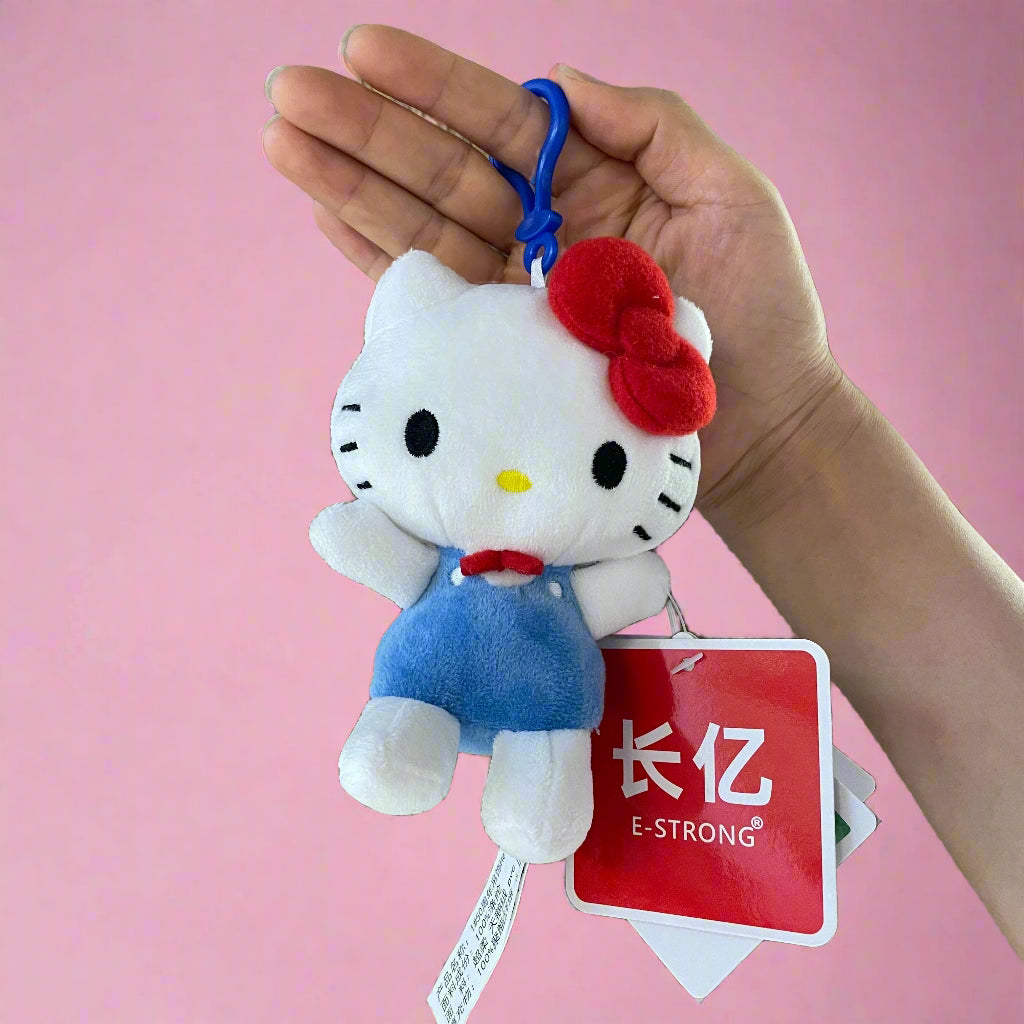 A plush toy of Hello Kitty wearing a blue outfit with a red bow and a keychain attached to it, celebrating the '50th Anniversary' of Hello Kitty.