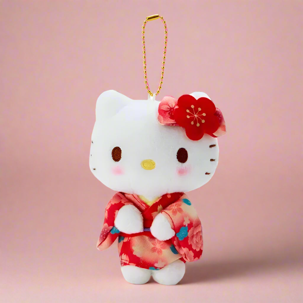 A plushie keychain of Hello Kitty wearing a green kimono with matcha theme, held in front of a shelf with various colorful toy figurines.